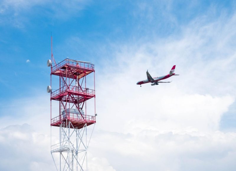 Airplane flying next to a red iron tower